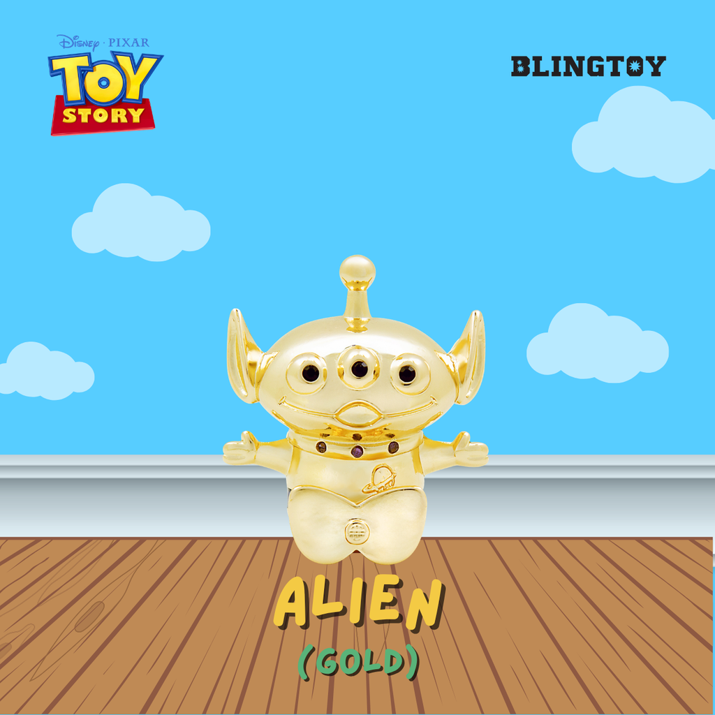 A gold-colored Blingtoy Alien collectible toy from Disney Pixar Toy Story, shown against a blue sky and wooden floor backdrop.