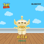 A gold-colored Blingtoy Alien collectible toy from Disney Pixar Toy Story, shown against a blue sky and wooden floor backdrop.