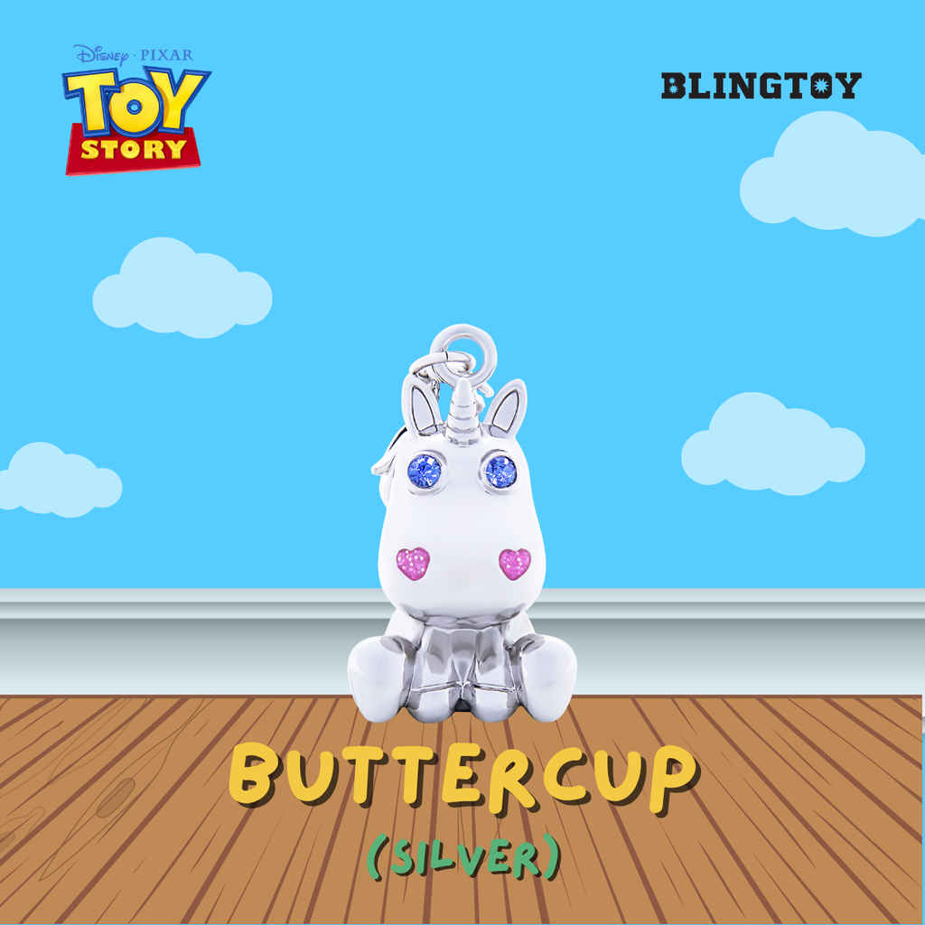 A silver-colored Buttercup unicorn keychain charm from Disney Pixar Toy Story, displayed on a wooden floor against a blue sky background with clouds. The image includes the Blingtoy brand logo in the top right and Toy Story branding in the top left.