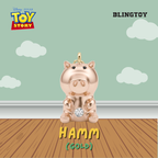 A gold-plated Hamm toy pendant from Disney Pixar Toy Story, shown sitting on a wooden floor against a mint green wall with clouds. The image includes 'BLINGTOY' branding and 'HAMM (GOLD)' text.
