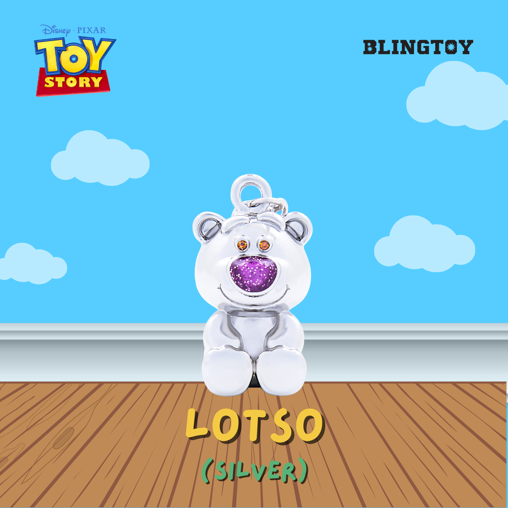 A silver Lotso bear charm from Disney Pixar Toy Story, featuring a glittery purple nose and orange eyes, displayed against a blue sky and wooden floor background. The image includes branding for Blingtoy and Toy Story.